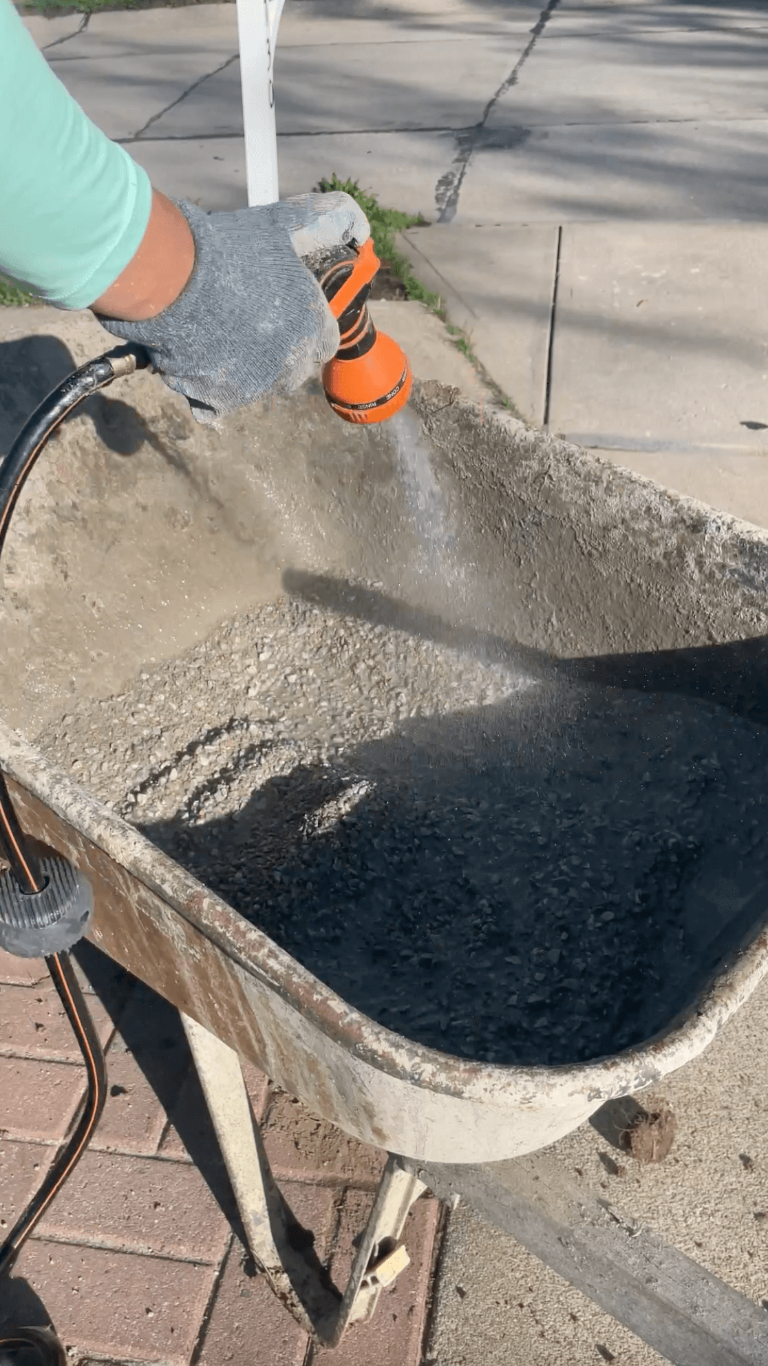 Adding water to mix concrete in a wheel barrow.